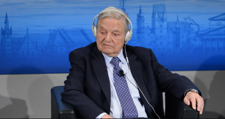 Elderly man in business suit wearing headphones during broadcast discussion about Soros raids India enforcement