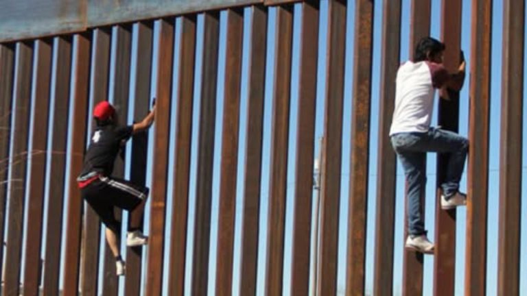 Poland border enforcement sovereignty defense: migrants climbing border fence barrier